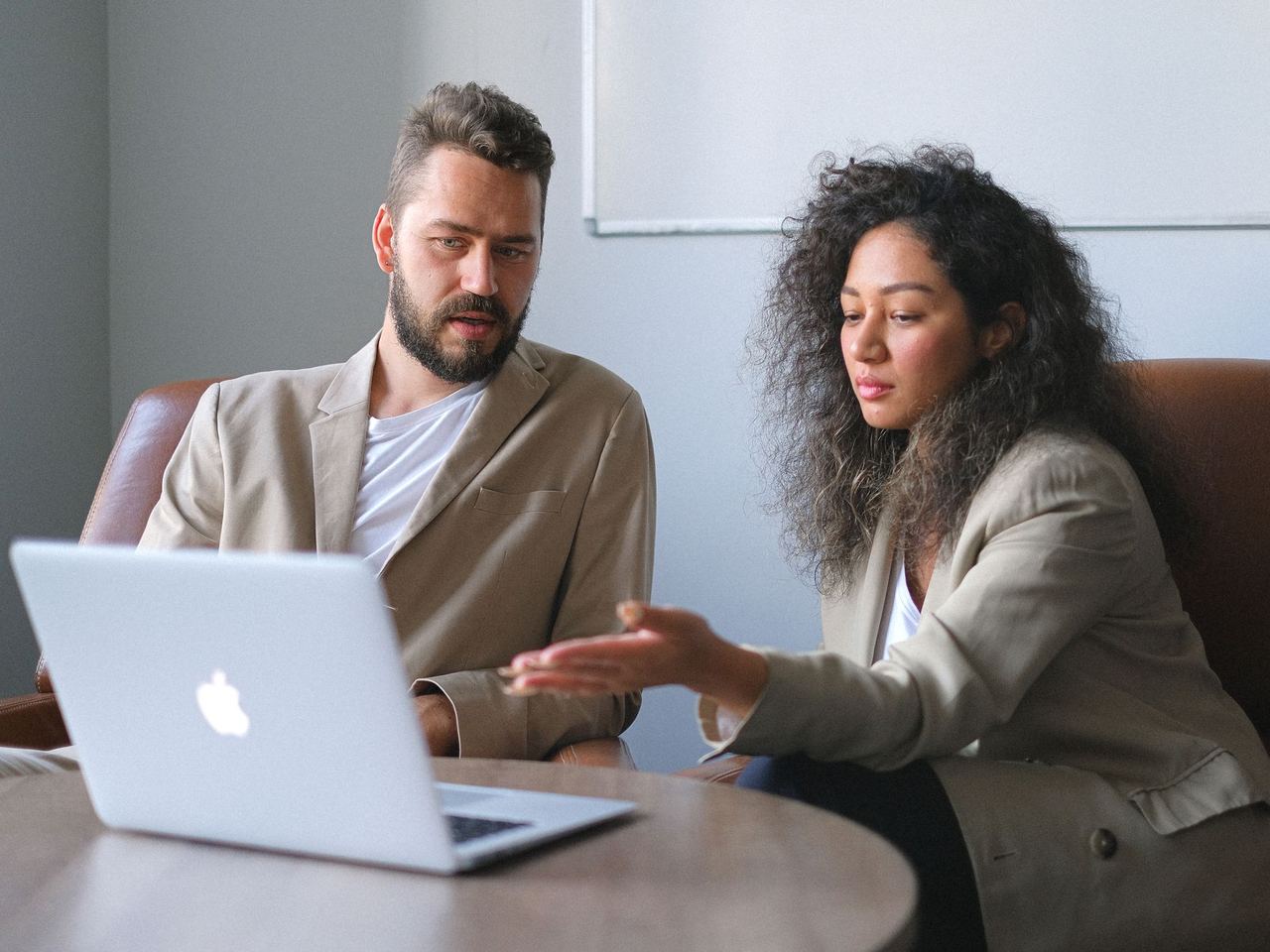Two colleagues talking across a laptop in a bright meeting room