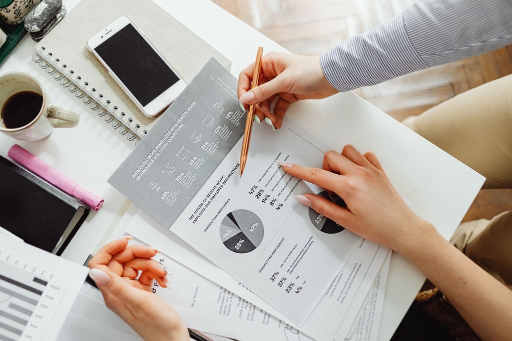 Two people at a desk reviewing printed charts and figures with a pen