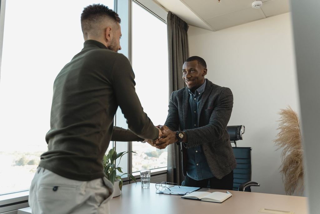 Two professionals shaking hands across a desk after a meeting