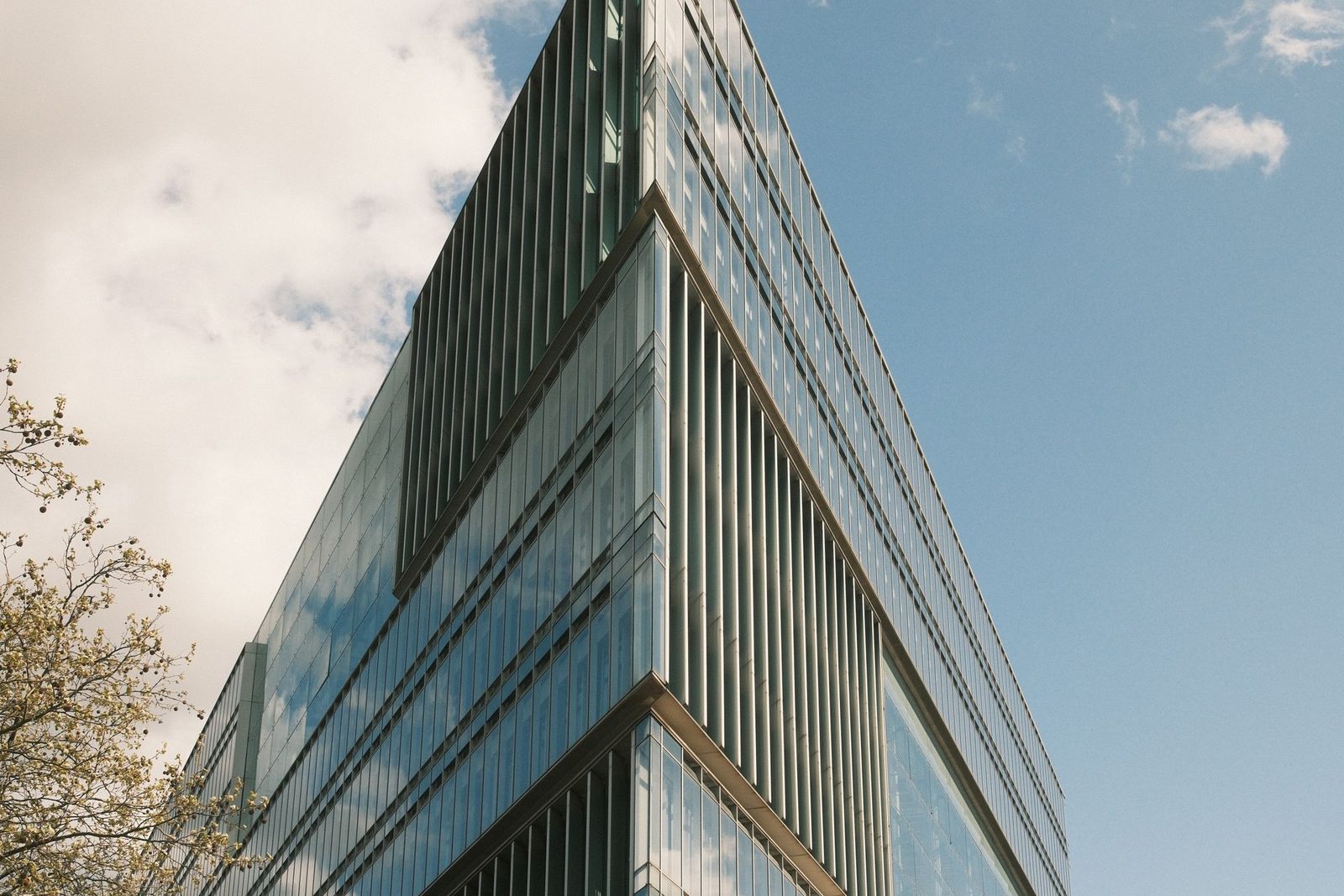 Modern glass office building with a sharp angular facade under a clear blue sky
